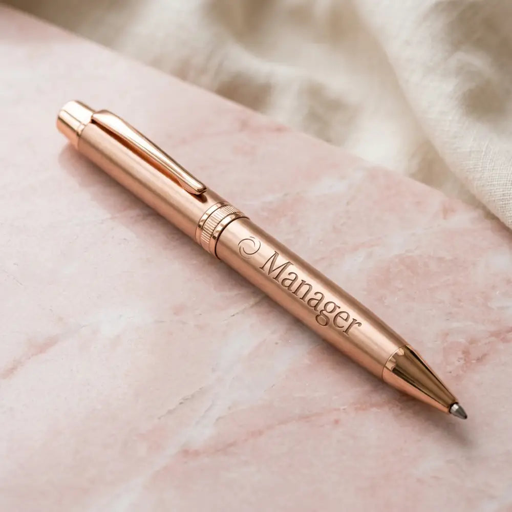 Rose gold pen with 'Manager' engraving on a marble surface