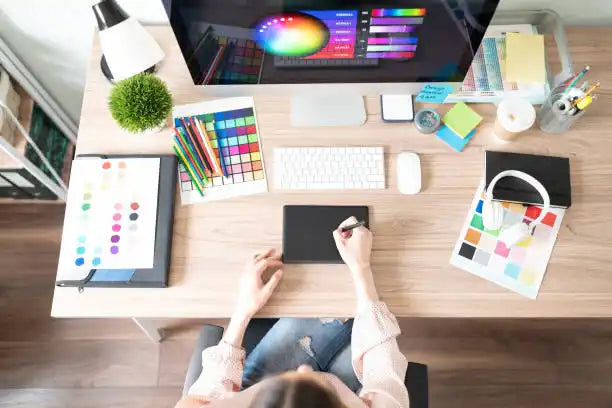 Overhead view of a graphic designer’s workspace with color swatches, digital tablet, and creative tools.