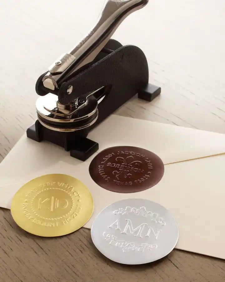 Embossing seal press with three metallic seal impressions in gold, silver, and bronze colors.