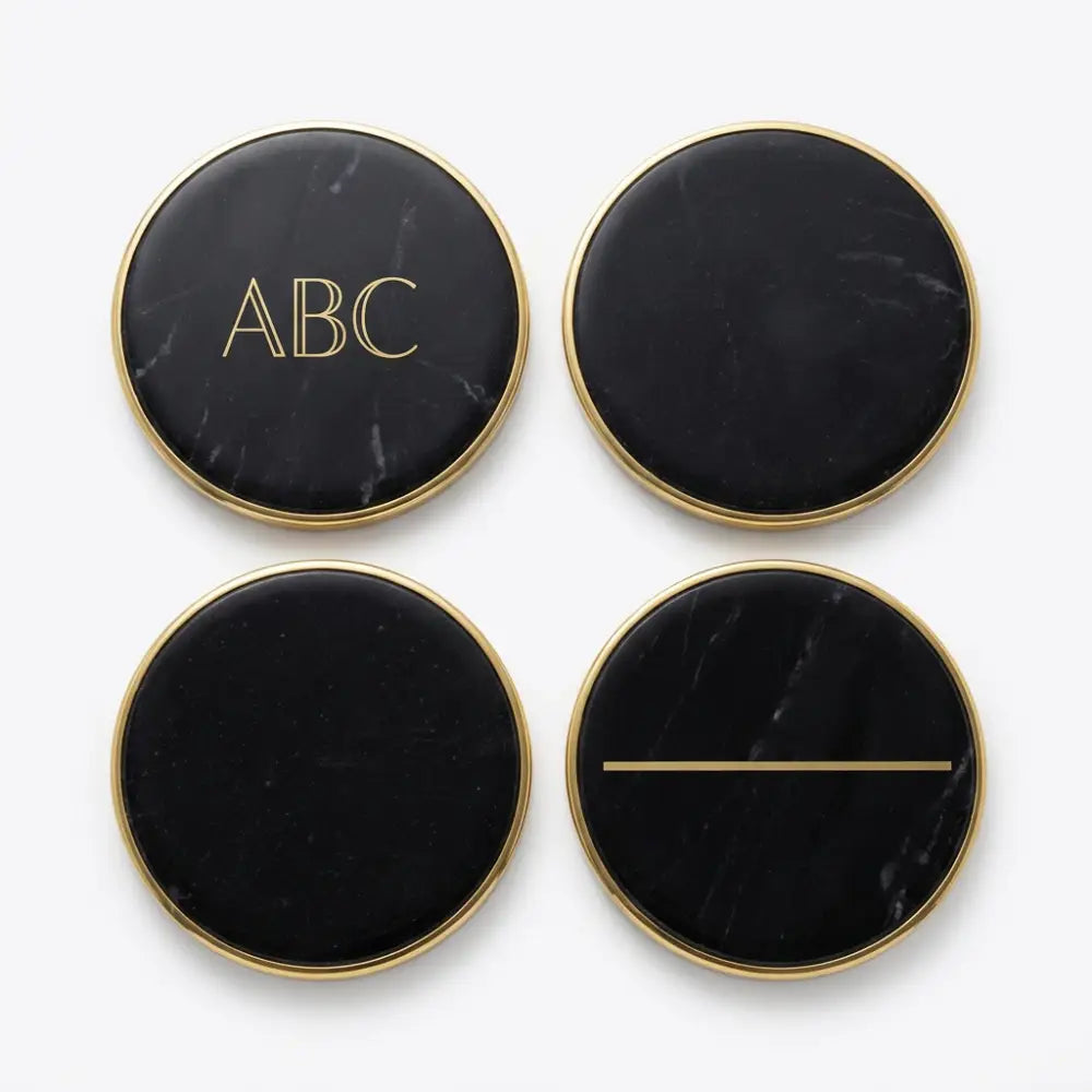 Four black marble coasters with gold edges and 'ABC' engraving on a white background